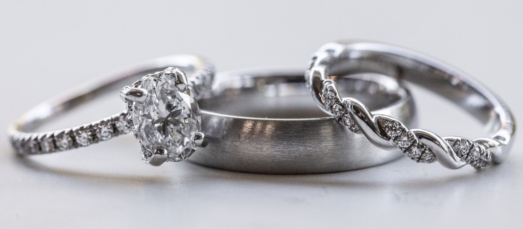 A silver wedding band and a diamond ring and engagement ring on a table