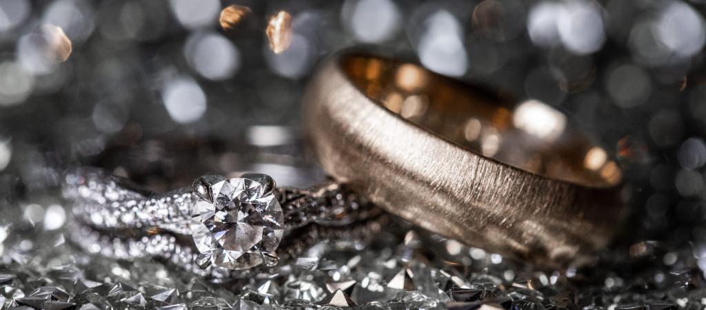 A gold wedding band and a diamond wedding ring sitting on a table. This is for the article called creative wedding ring engraving ideas