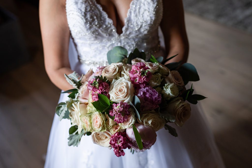 A purple, blush, and white bridal bouquet being held by the bride