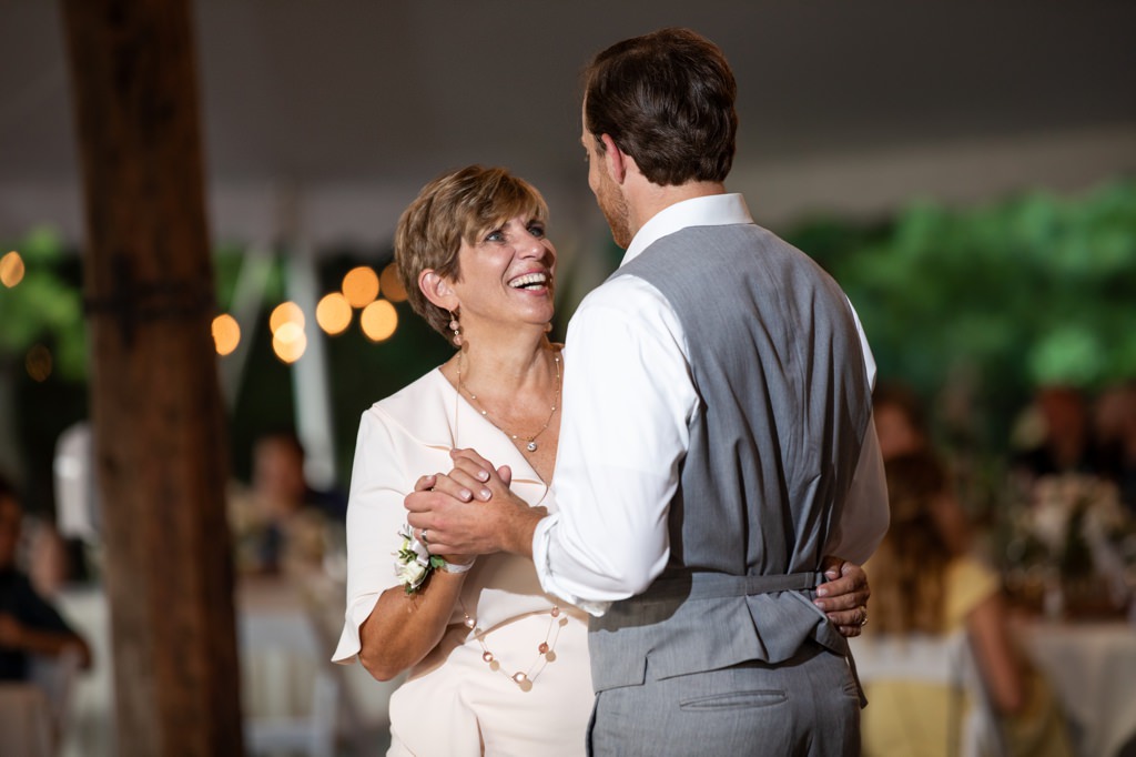 A mom smiling at her son as they share a mother-son dance at his wedding