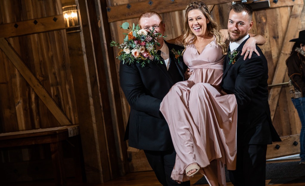 Two groomsmen carrying a bridesmaid during the wedding party intros