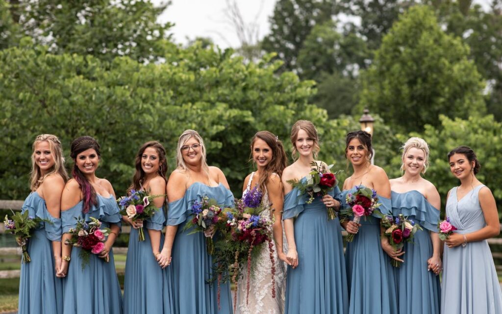 A bride and bridesmaids wearing blue dresses posing. This is for the blog post called how to plan a wedding for 10,000 or less