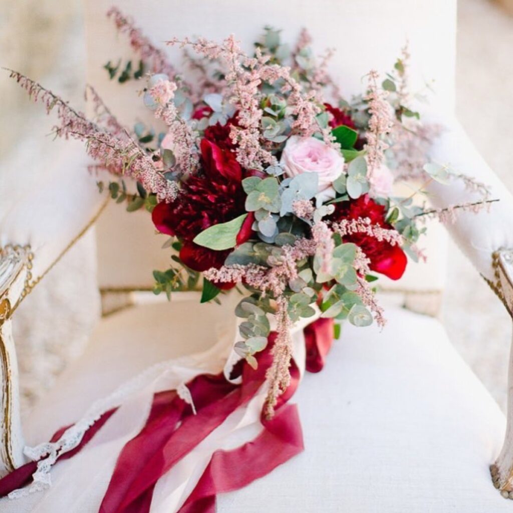 A wedding bouquet sitting on a chair with red ribbon