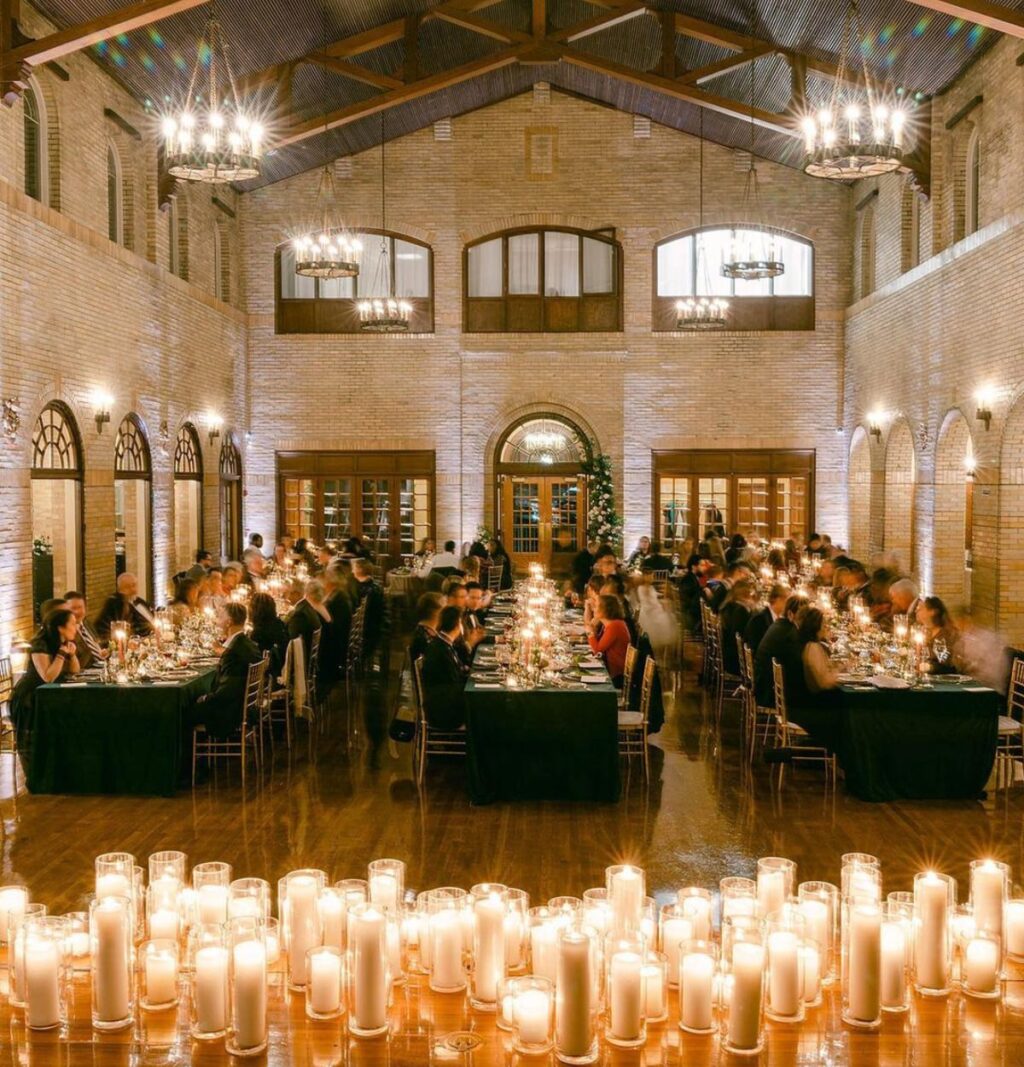 Three long wedding reception tables with guests eating at candlelit tables.