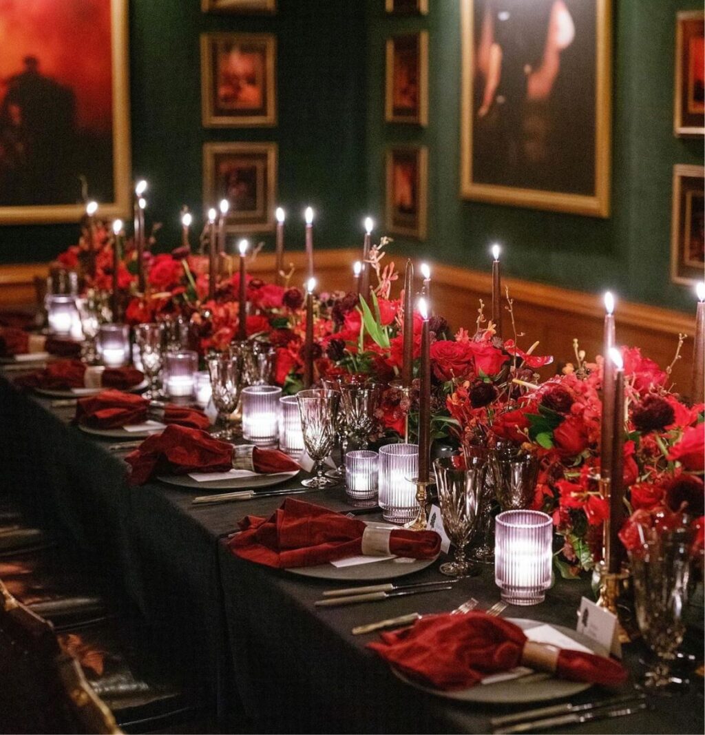 A winter wedding reception table decorated with red flowers and tall candles.