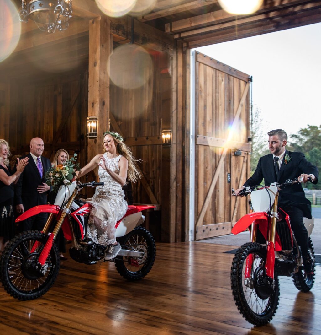 Bride and groom riding to their wedding reception on red Honda dirt bikes. 