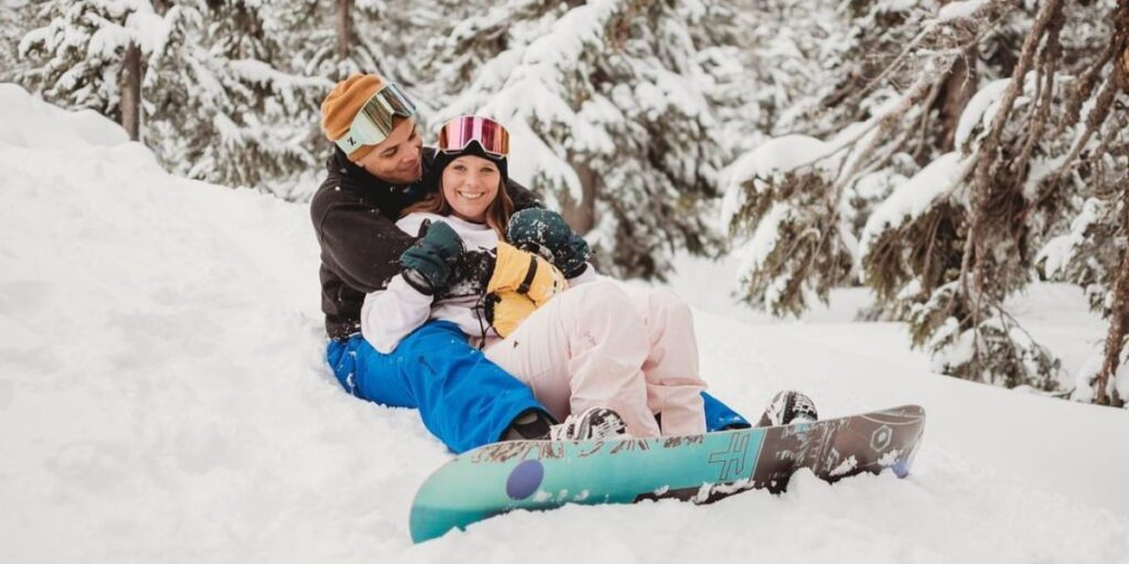 A couple posing for a photo in the snow with their snowboard