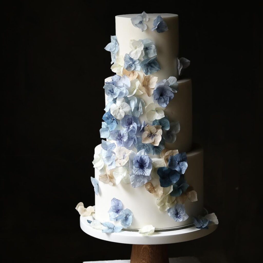 A three-tier winter wedding cake with blue and silver flowers.