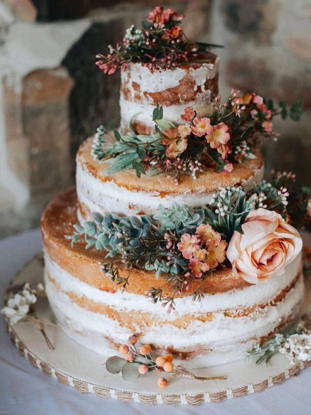 A semi-naked winter wedding cake with 3 tiers. Lots of boho styles decorations like sprigs of berries and evergreen and flowers with soft blush colors.