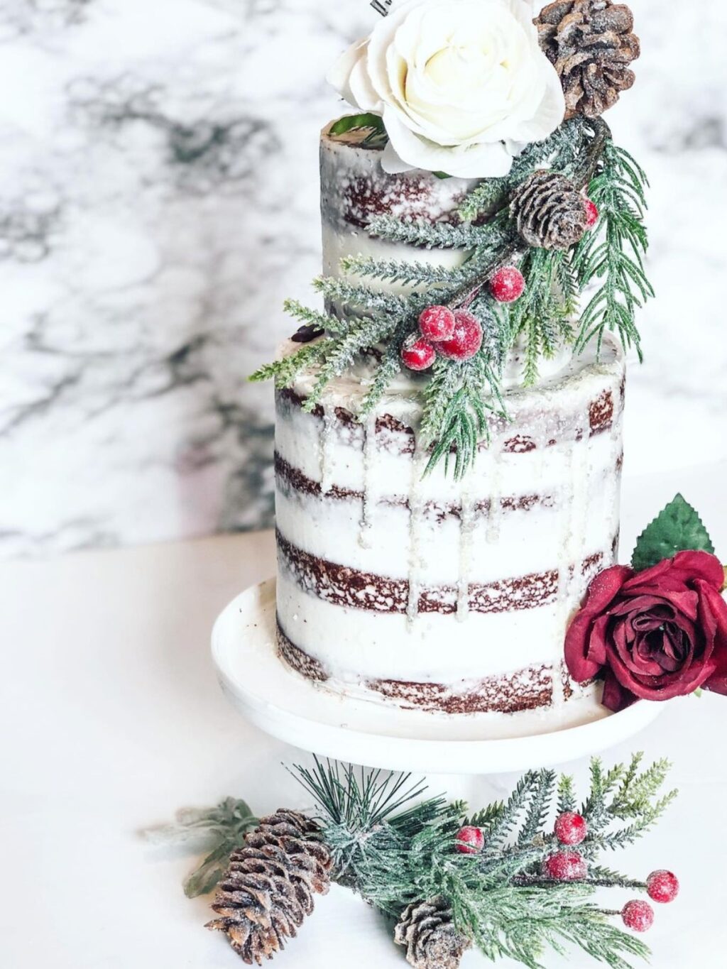 A semi naked winter wedding cake with cranberries, pinecones, and pine tree sprigs