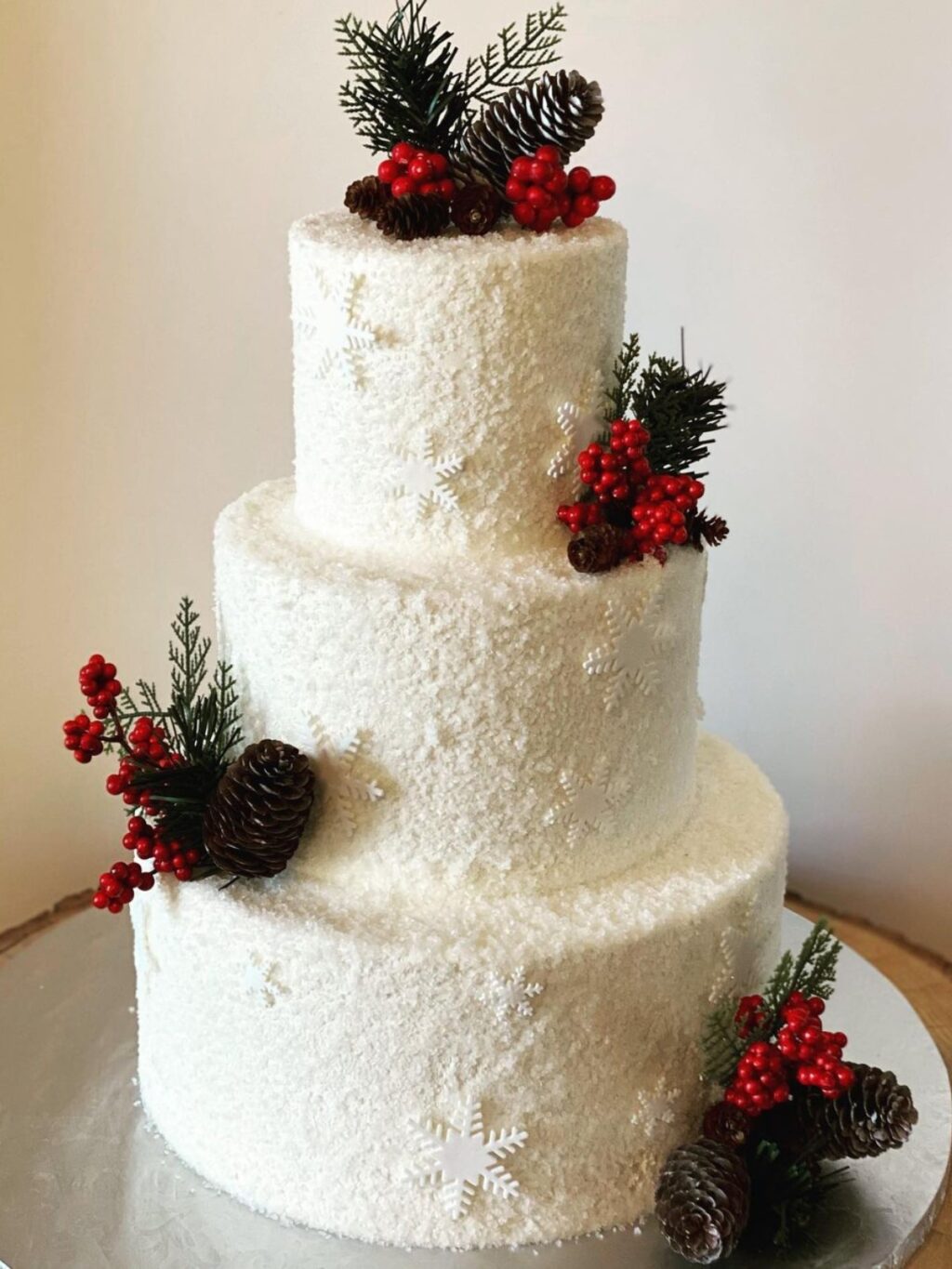 A 3-tier white wedding cake with pinecones and red berries