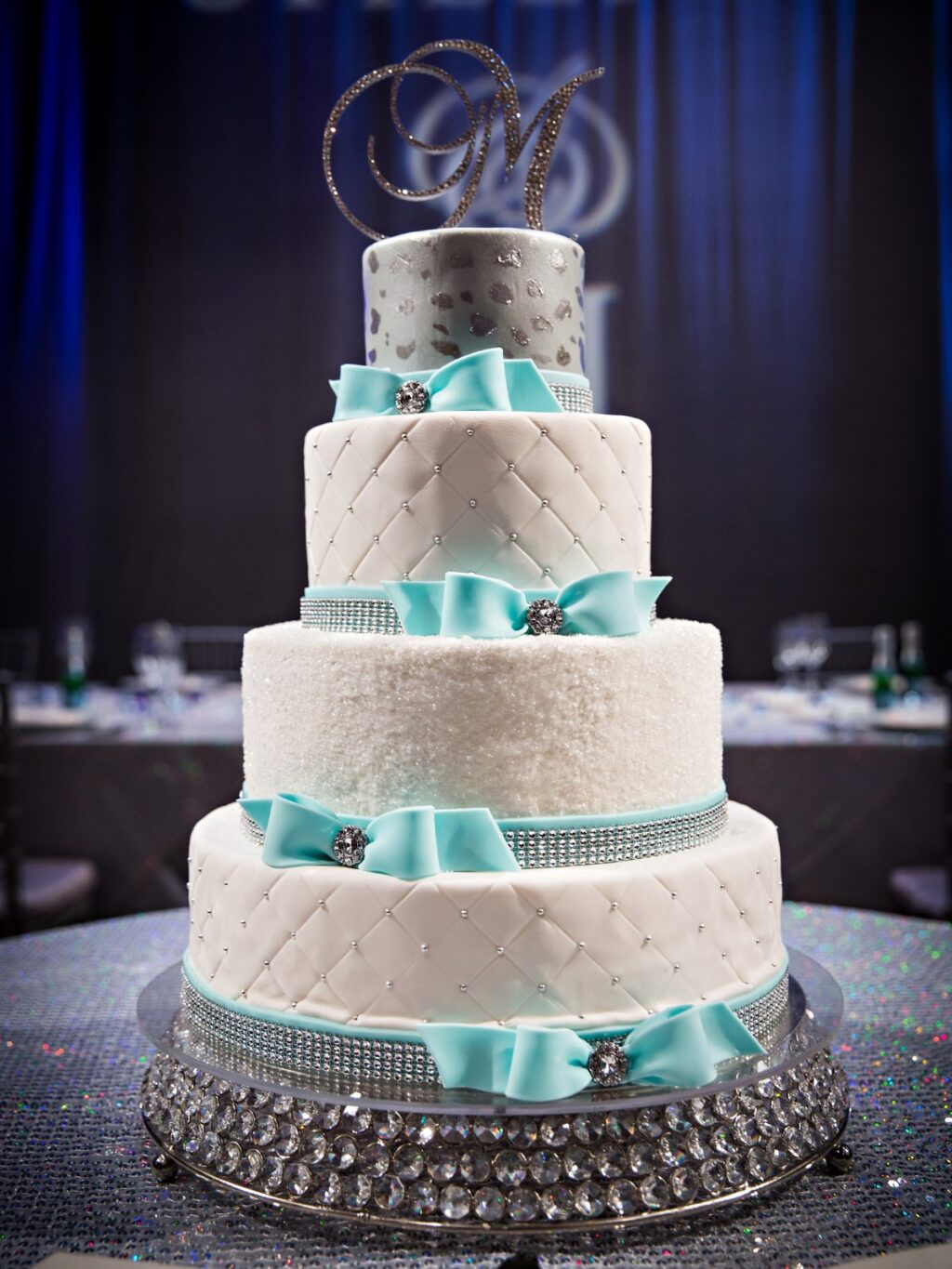 A 5 tier white winter-themed wedding cake with tiffany blue bows and silver sparkle decorations