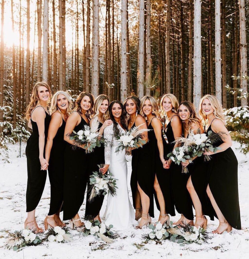 A bride and bridesmaids posing outdoors in the middle. They are wearing black dresses. There is snow on the ground