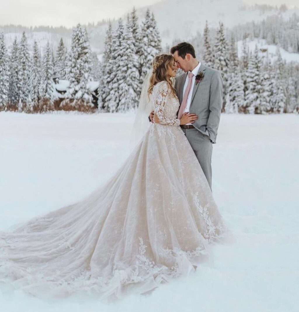 A romantic wedding photo of a bride and groom posing in the snow with snow covered trees in the background