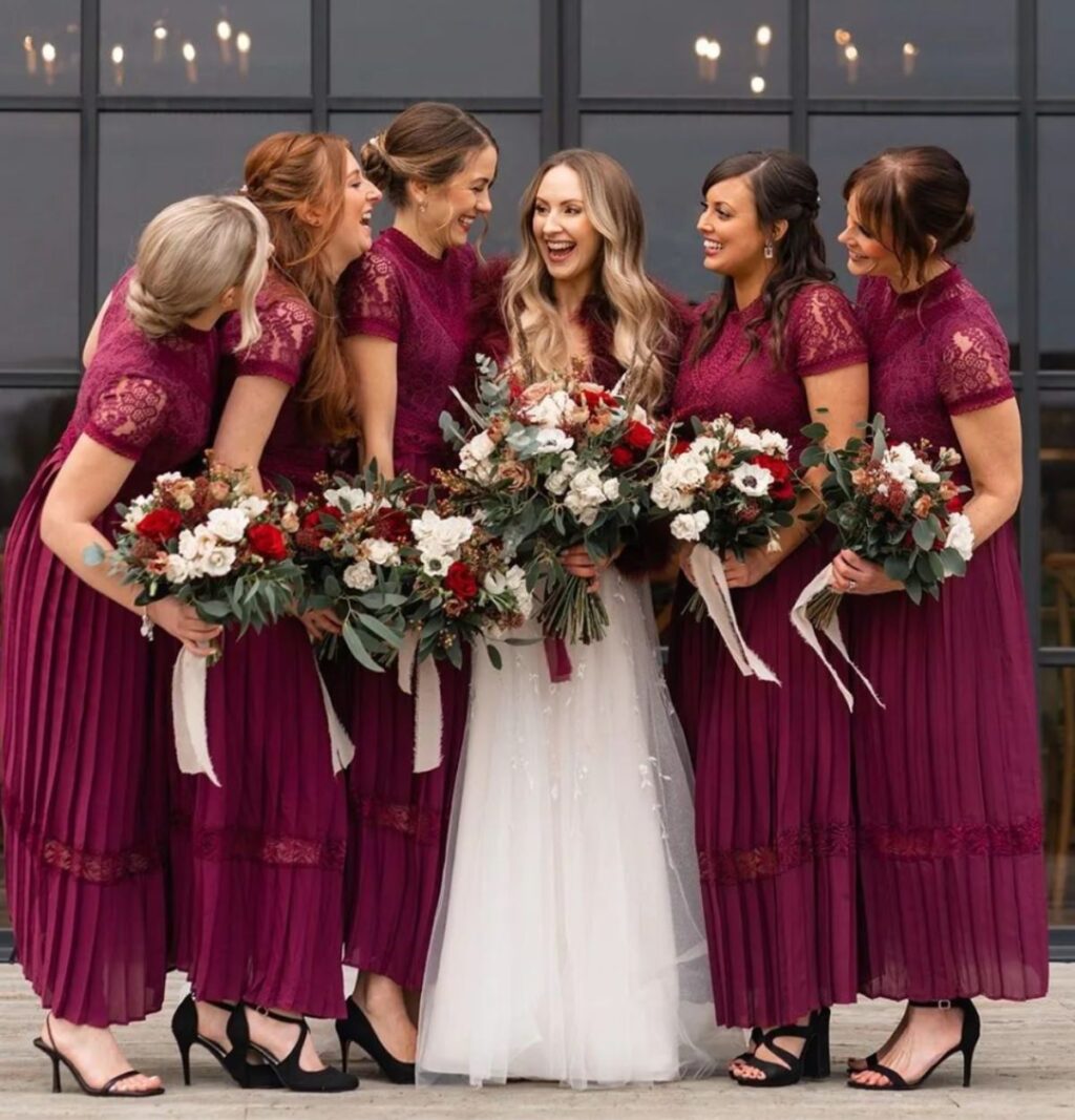A bride and bridesmaids who are wearing burgundy red bridesmaid dresses are posing in the winter with their bouquets.