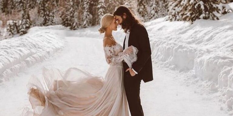 A bride and groom posing in the middle of a snow covered road in the middle of winter