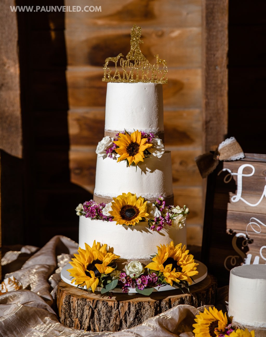 A 3-tier white rustic wedding cake in a barn with yellow sunflower decorations