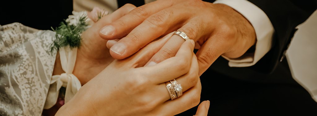 A close up photo of a bride putting a wedding ring on a groom