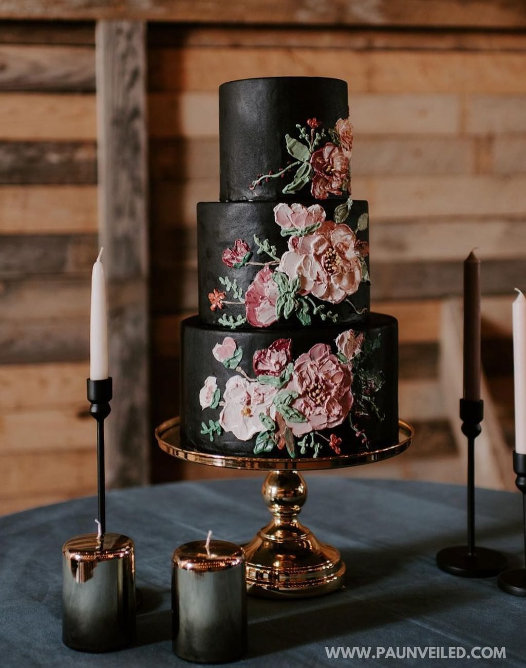 A 3-tier moder-rustic wedding cake with black frosting and pink decorative flowers