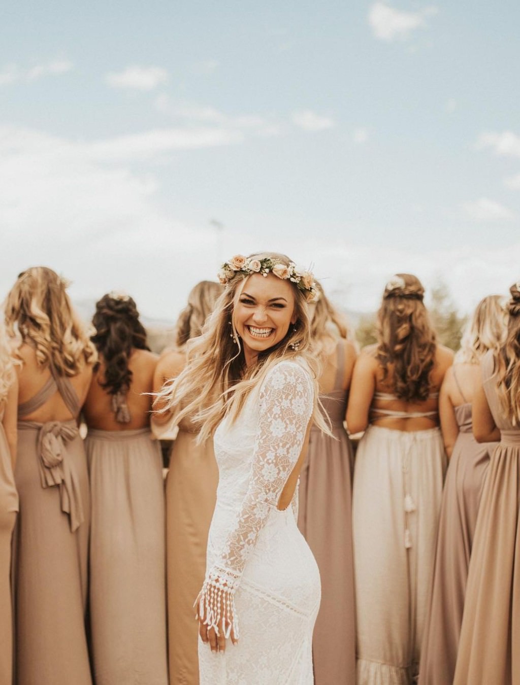A beautiful bride smiling for the camera and the bridesmaids are in the background with their backs to the camera.
