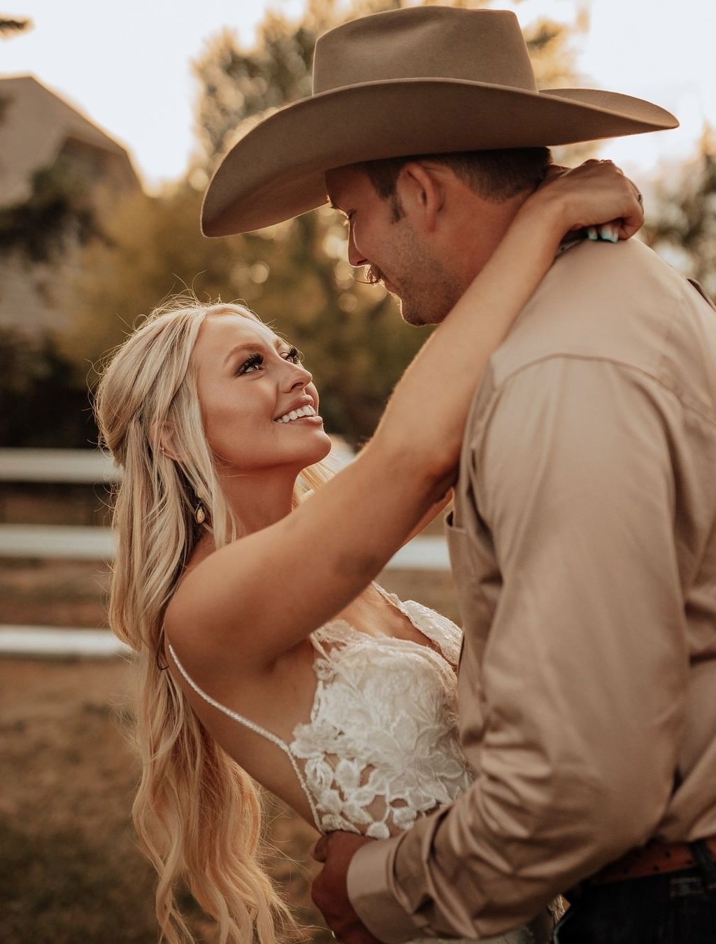 A beautiful bride smiling at the groom. she has her hands around his shoulders and he is wearing a cowboy hat.