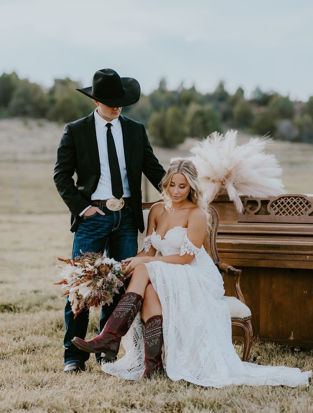 A bride and groom posing near an antique piano in a field.