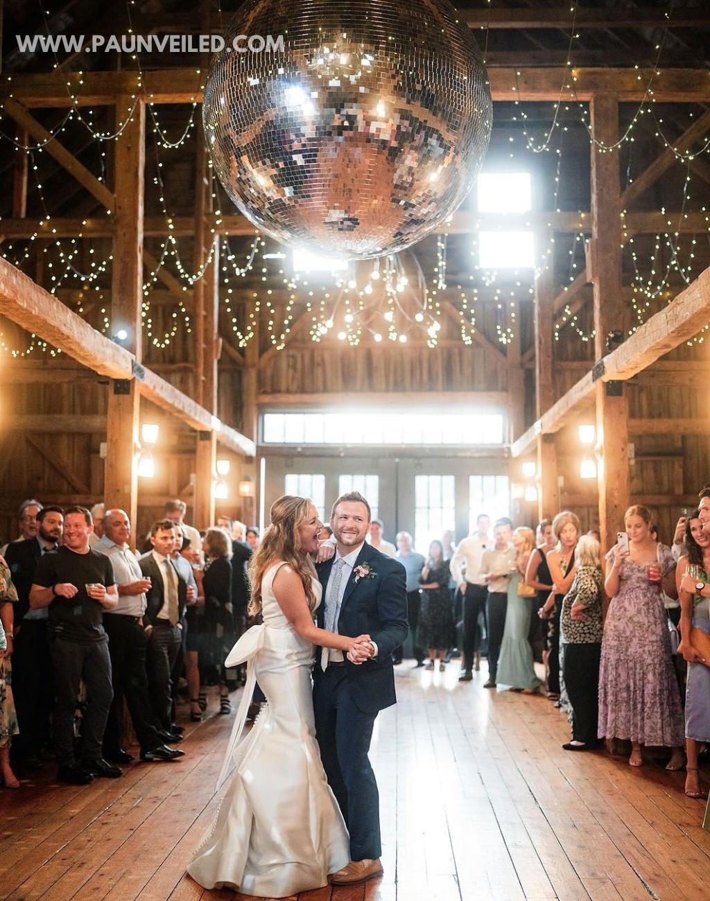 A bride and groom doing their first dance in a rustic barn with a disco ball