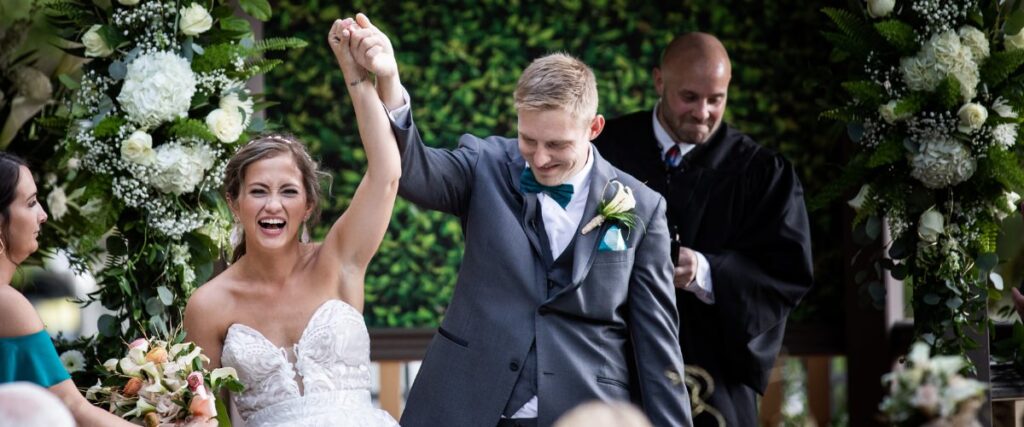 A bride and groom raising their hands in the air after getting married. This is for the blog post called how to save money on wedding photography