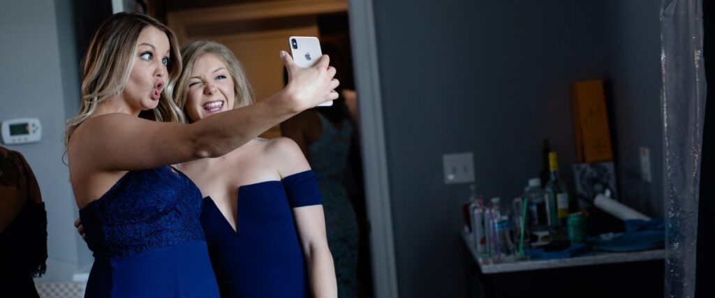 Two funny bridesmaids taking a selfie together and making funny faces