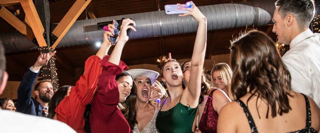 A wedding guest taking a selfie with the bride and some other guests while they are in the middle of the dance floor at the wedding reception.