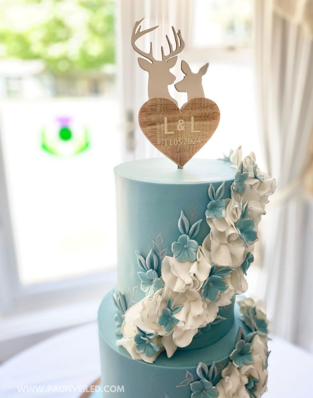 A 2-tier blue wedding cake with editable sugar flowers and a deer antler cake topper