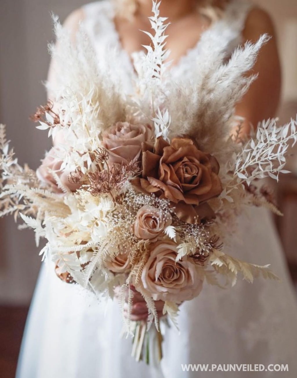 A rustic bridal bouquet with blush and beige tones being held by the bride in her white dress