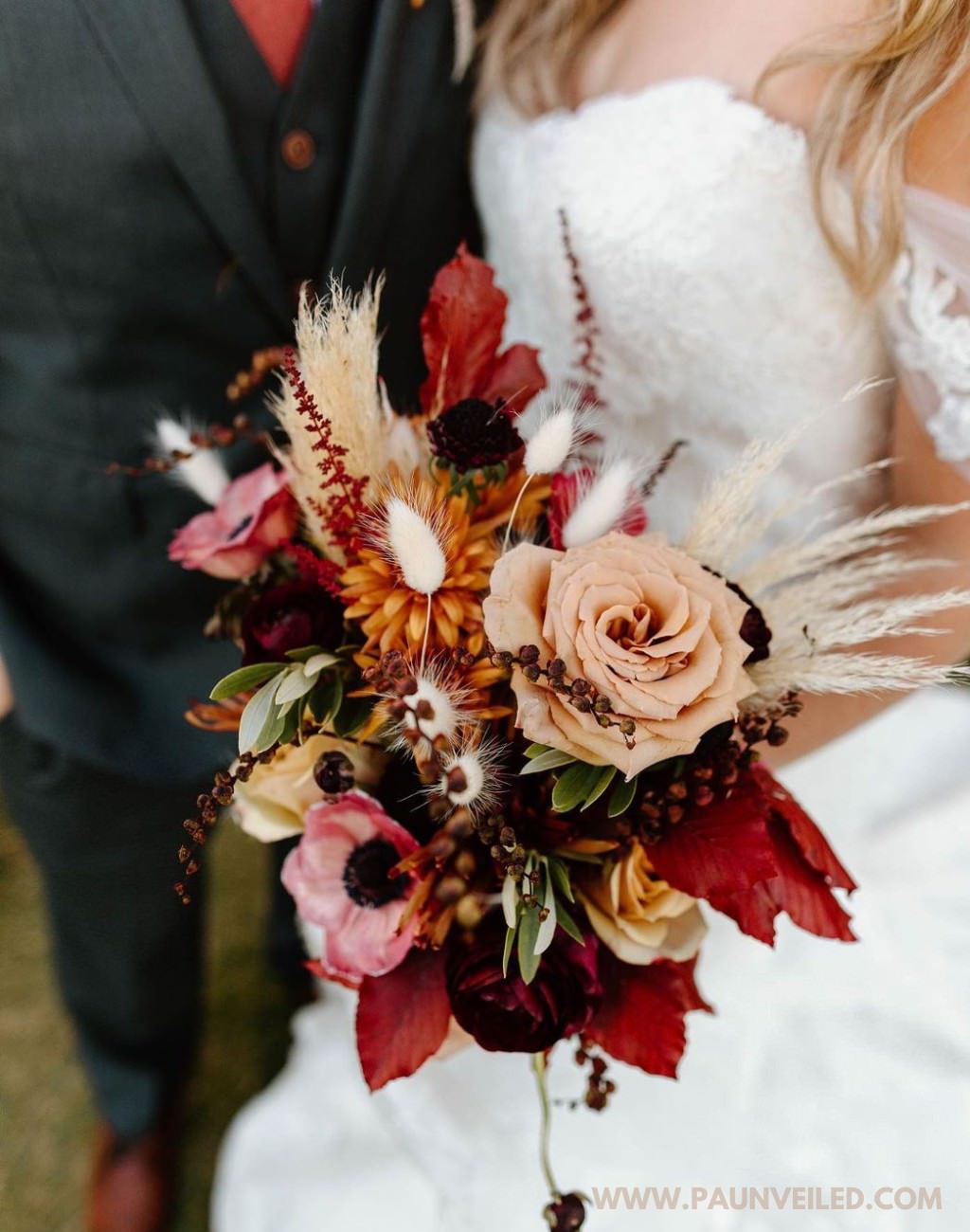 A red, orange, and rust colored rustic wedding bouquet being held by the bride