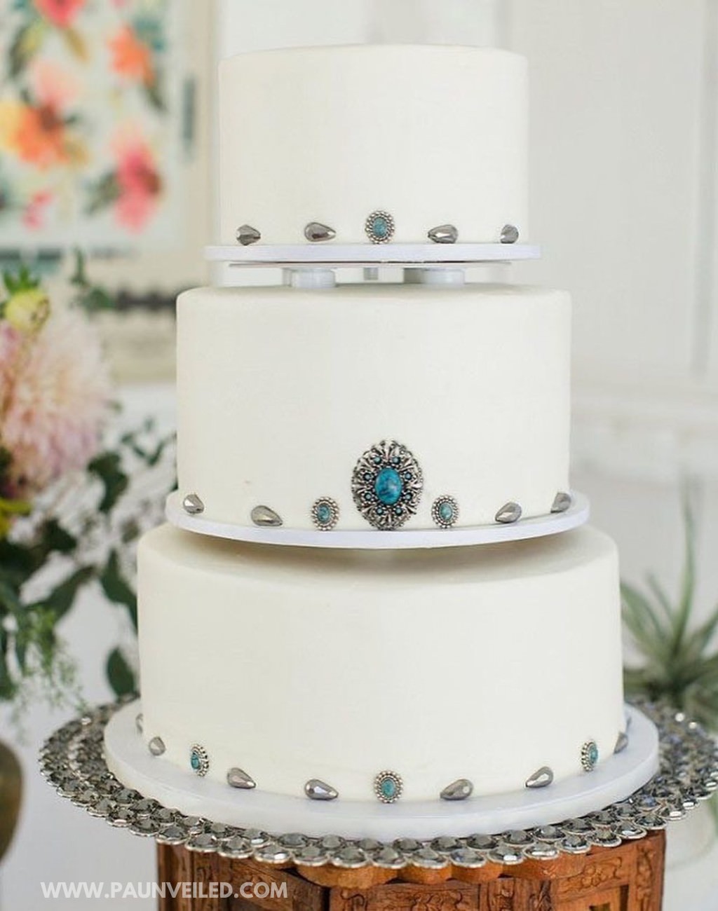 A 3-tier white rustic country-western wedding cake with turquoise ornaments on it
