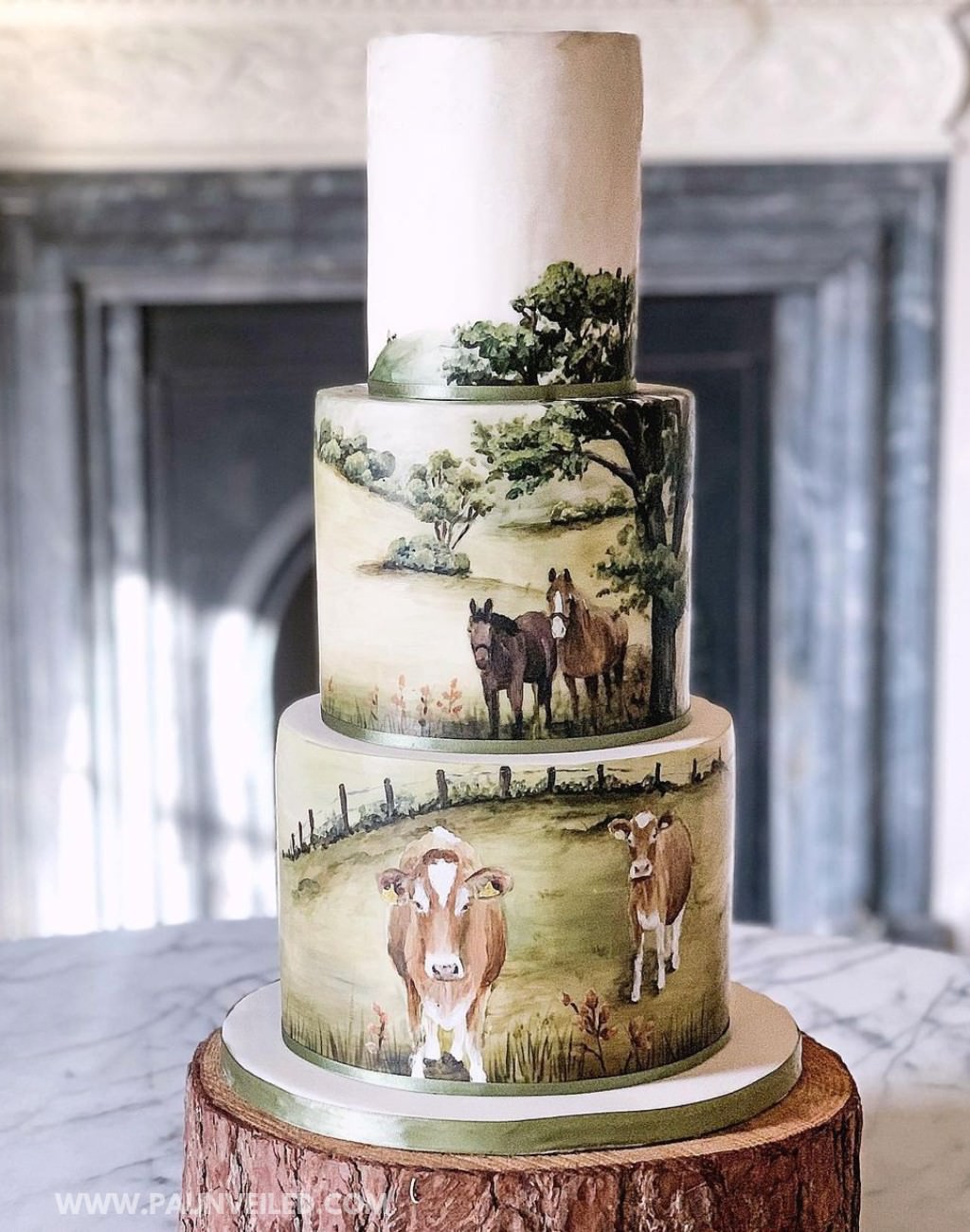 A modern 3-tier rustic wedding cake with hand-painted farm scenes featuring cows and horses.