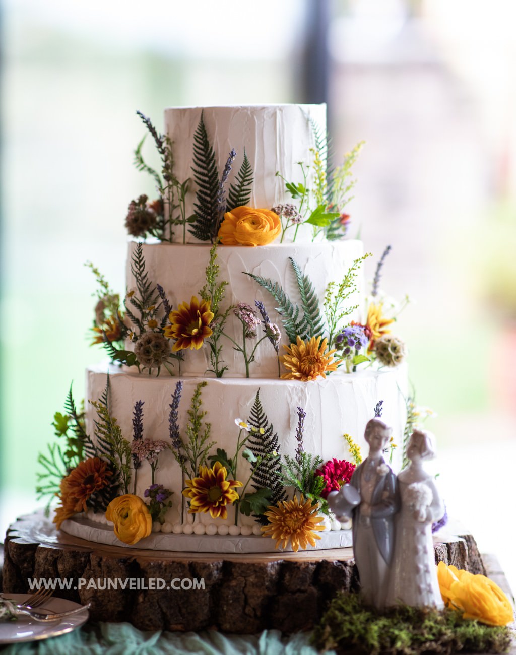 A 3-tier wedding cake with white frosting and fresh wildflowers