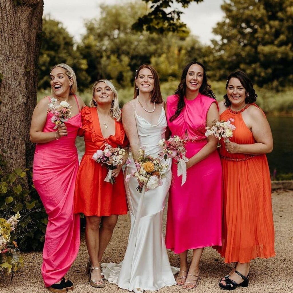 A photo of a bride with her bridesmaids. The girls are wearing orange and pink bridesmaid dresses