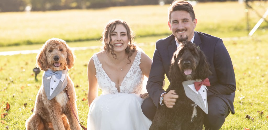 A bride and groom posing with their two dogs who are wearing little vests on the wedding day