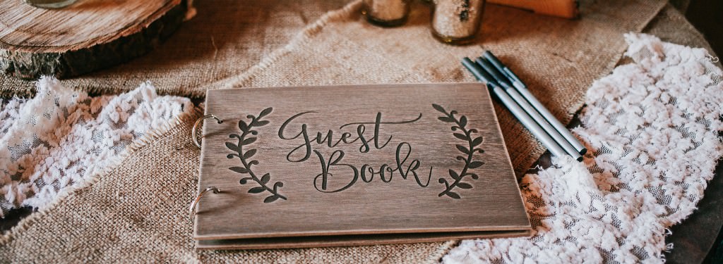 A wedding guest book and 3 pens on a table
