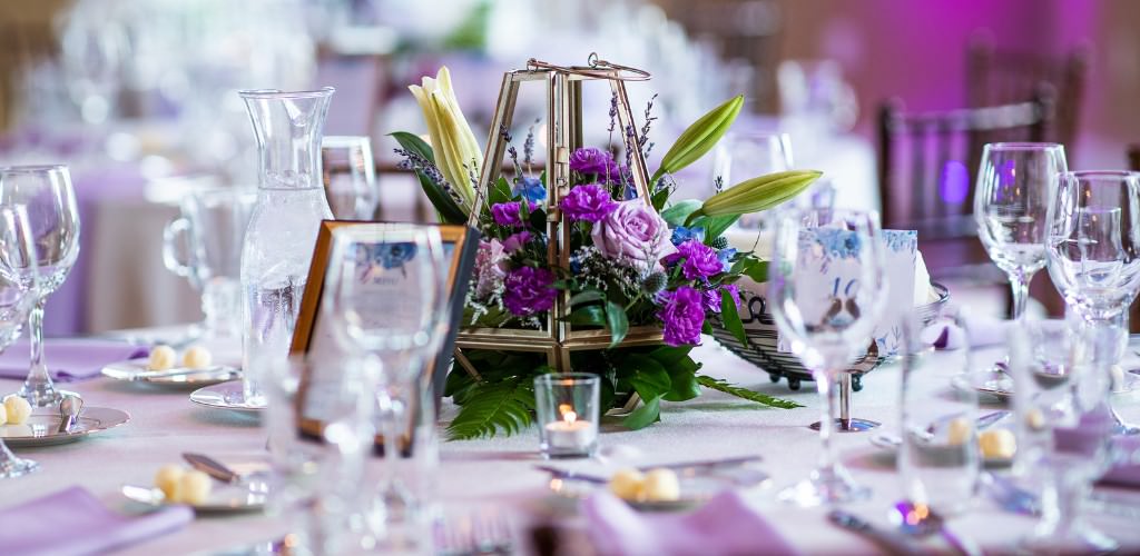 A wedding centerpiece made with fake purple flowers. This is for the article called wedding planning hacks to save you money