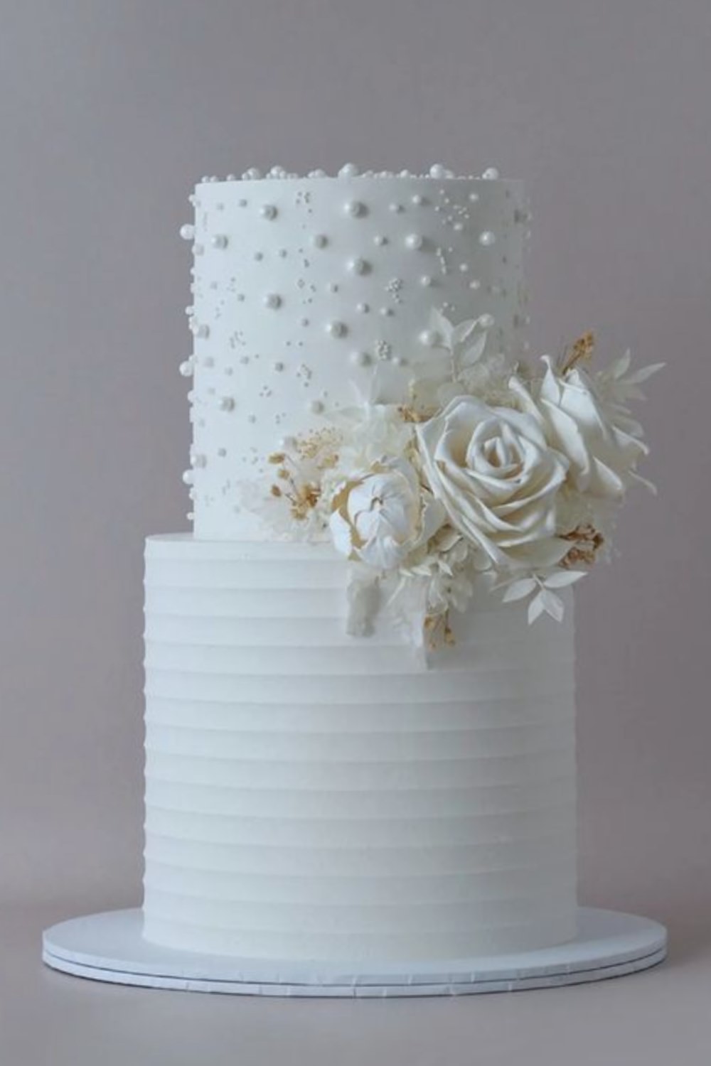 An all white two-tier wedding cake design with sugar flowers