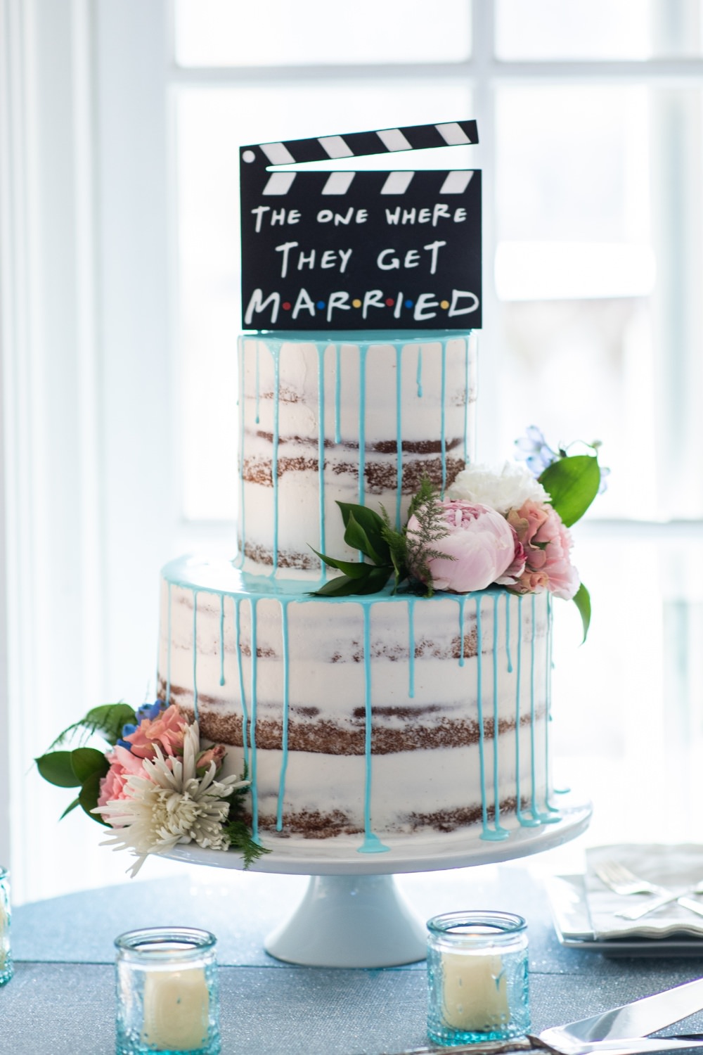 A fun semi-naked-two-tier wedding cake with blue drizzle and a Friends TV show theme cake topper
