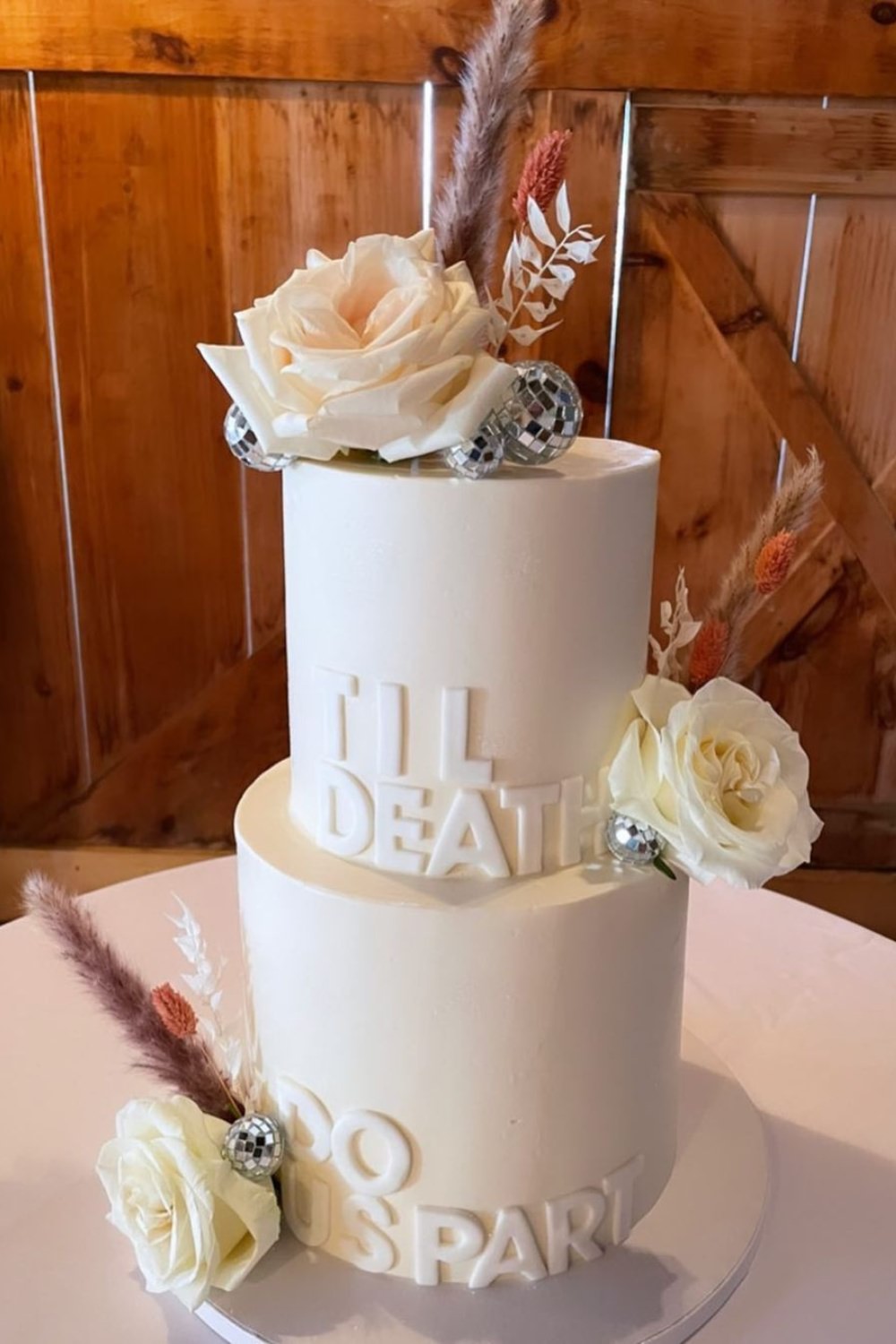 A fun and modern white two-tier wedding cake with Til Death Do Us on it