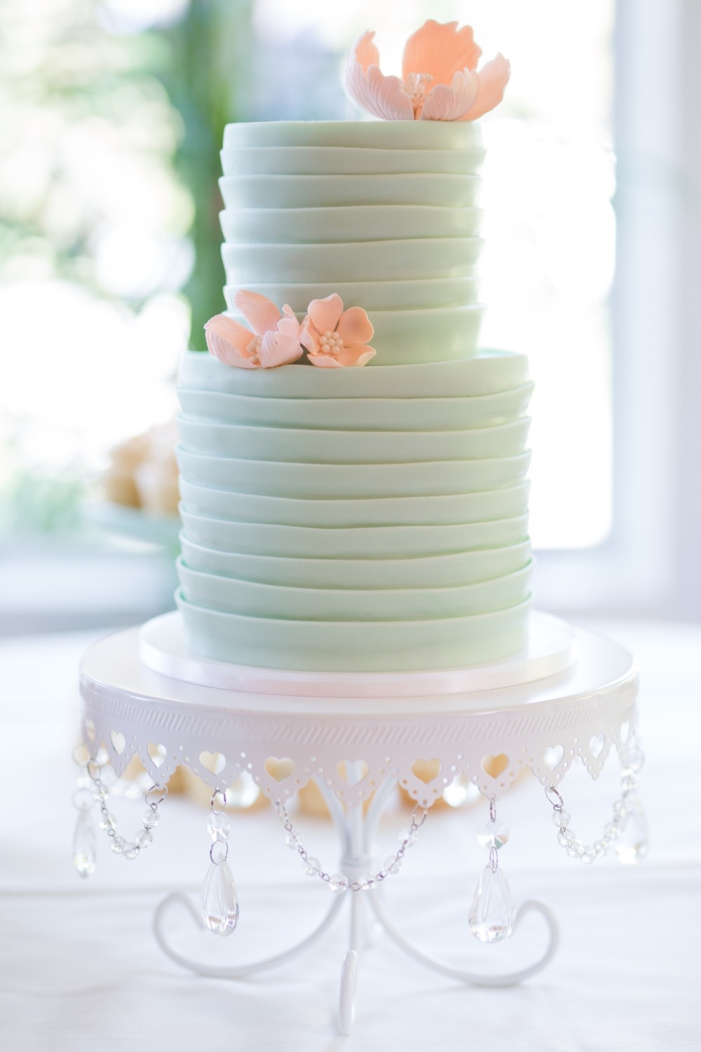 A pretty 2-tier wedding cake design with light green frosting fondant and pink peach flowers