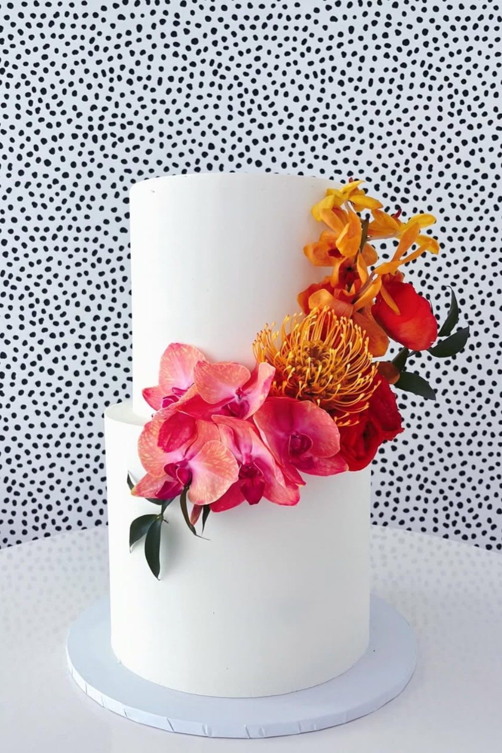 A pretty white two-tier wedding cake with red and orange flowers