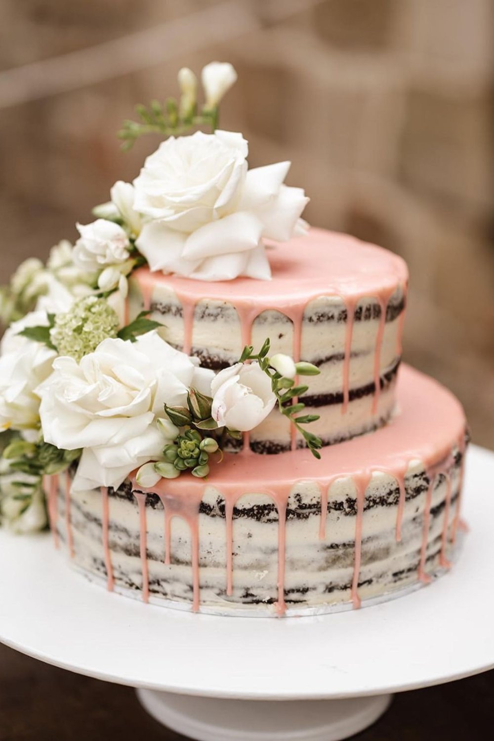 A semi-naked rustic wedding cake with pink drizzle
