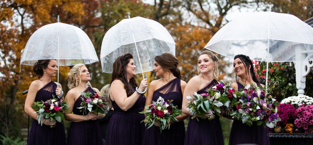 Bridesmaids standing outside in the rain with clear umbrellas
