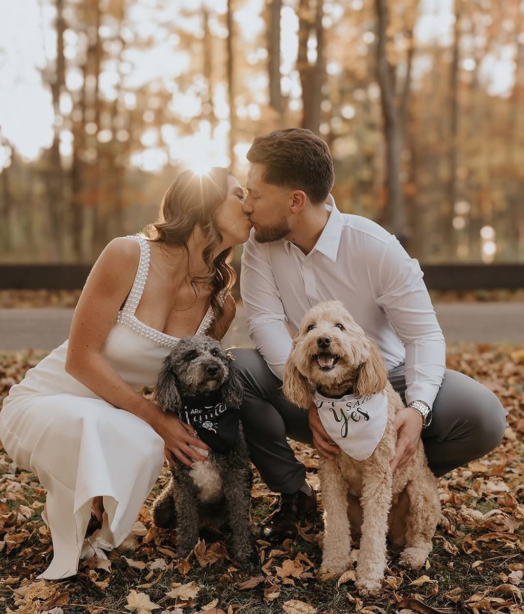 A couple kissing as they pose for engagement photos with their two dogs