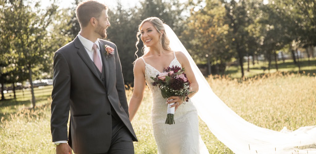 A bride and groom walking through a field