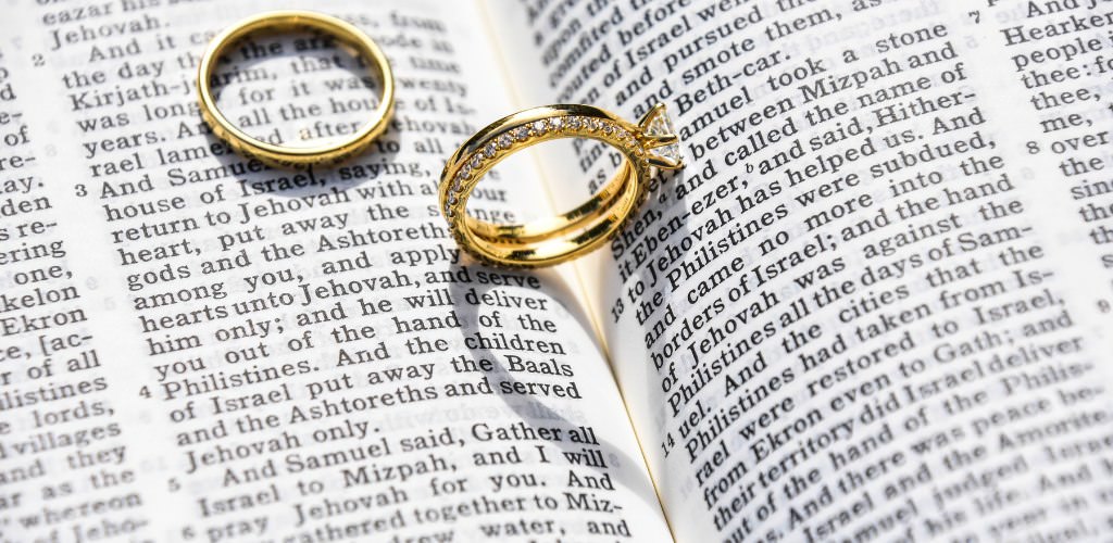 Two wedding bands inside a Bible making a heart shadow on the pages